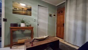 Ein Wohnzimmer mit Couch, einem Holztisch, einem kleinen Tisch mit Pflanze und einer Tür mit Fenster.