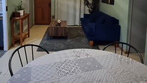 Ein Wohnzimmer mit Esstisch, blauem Sofa, Couchtisch aus Holz und einer Deckenleuchte.