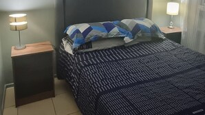 Ein Schlafzimmer mit einem Bett, einem Nachttisch mit Lampe, einem Deckenventilator und einem Bild vom Eiffelturm an der Wand.