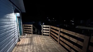 Una terraza de madera con barandilla, una puerta y una fuente de luz.