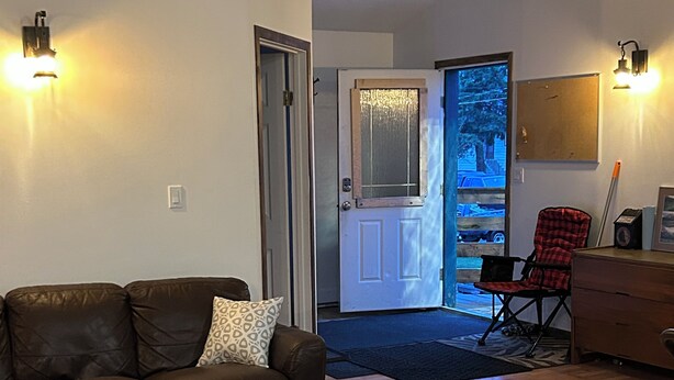 Una sala de estar con un sofá, una mesa de centro y un tapete estampado. Una puerta da a un balcón con vistas al exterior.