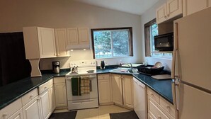 Cocina compacta con armarios blancos, encimera negra, estufa, microondas y refrigerador.