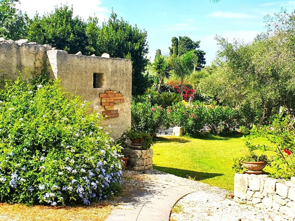 Un giardino con un muro in pietra, un vialetto e diverse piante.