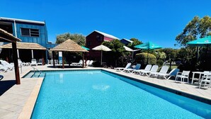 Una piscina rectangular con agua cristalina y azul, rodeada de sillas de descanso y sombrillas.