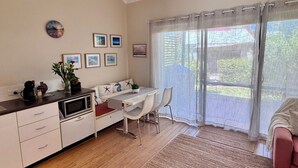 Un espacio habitable compacto con kitchenette, comedor y un ventanal con cortinas ligeras.