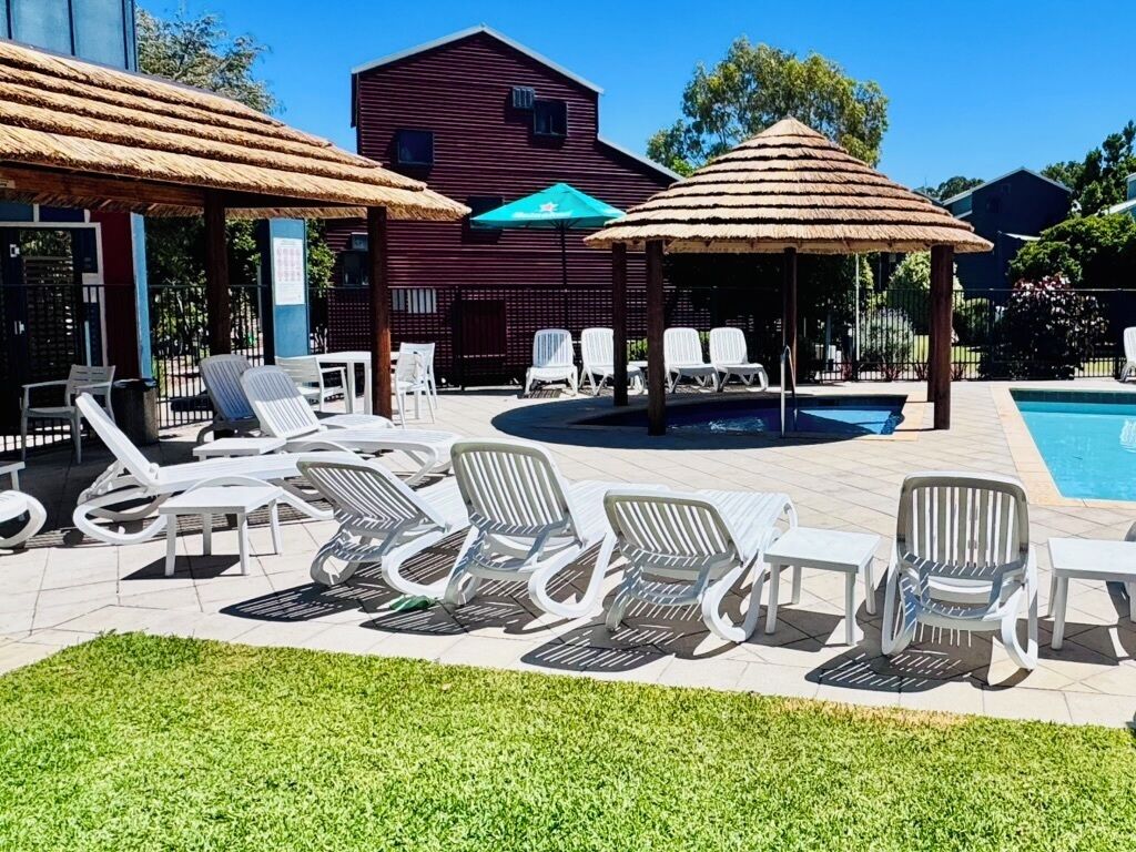 A pool area with lounge chairs and umbrellas, a building in the background, and a clear blue sky.