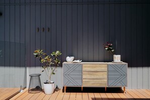Ein moderner Außenbereich mit Holzterrasse, einem Metallstuhl, einem Topfpflanzen und einem dekorativen Schrank mit geometrischen Mustern.