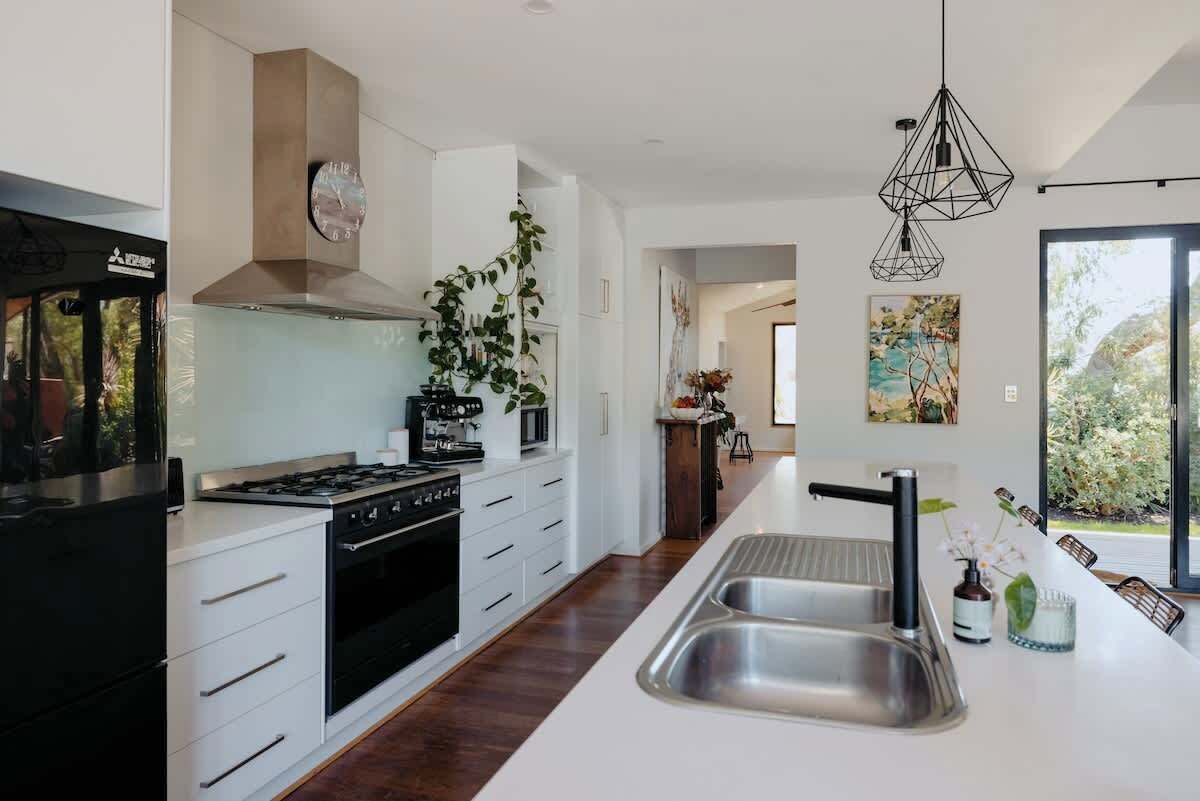 Una cocina moderna con estufa a gas, horno, armarios blancos, una isla grande con lavamanos e iluminación colgante.