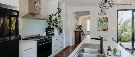 Una cocina moderna con estufa a gas, horno, armarios blancos, una isla grande con lavamanos e iluminación colgante.