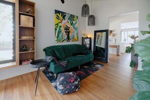 Un salón con un sofá verde, una mesa redonda, una estantería y dos lámparas colgantes.