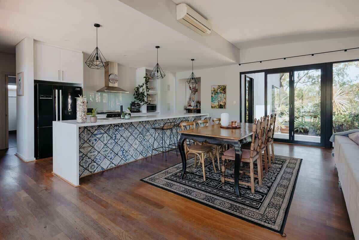 Uma cozinha moderna com ilha central, eletrodomésticos pretos e luminárias pendentes.