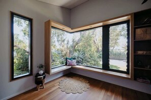A room with a corner window seat, a small side table with a plant, and a wooden floor. - Coastal Heights—Stylish Pool Paradise for Families (Dunsborough)