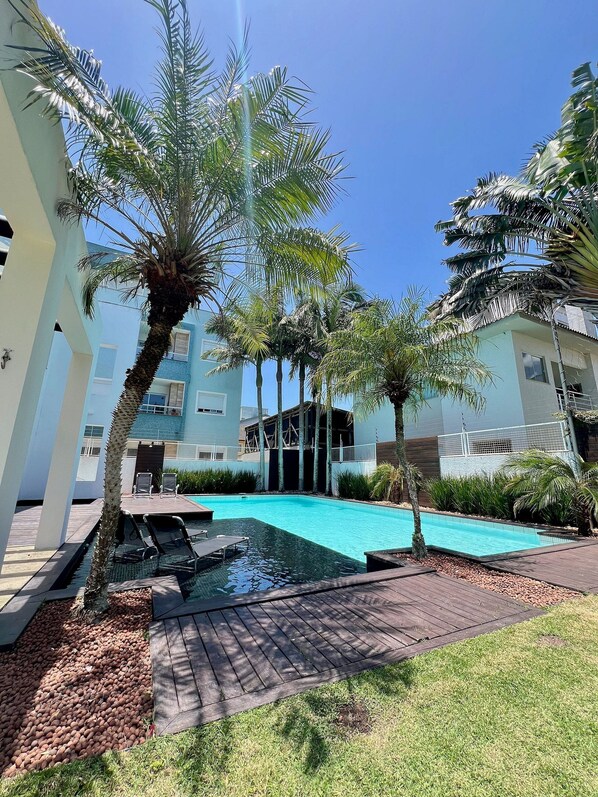 A swimming pool surrounded by palm trees and a building with a modern design. - Casa Ingleses (Florianópolis)