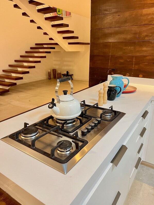 A kitchen with a gas stove, a kettle, and a blue pitcher on the counter. - Casa Ingleses (Florianópolis)