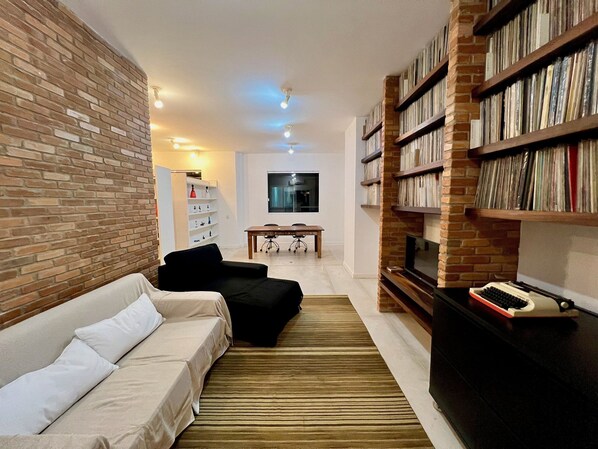 Un salon avec un mur en briques, un canapé, une bibliothèque et un téléviseur.