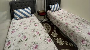Una stanza con due letti, un tavolino, una lampada decorativa a soffitto e una finestra con tende.