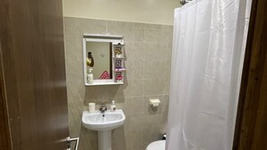 Un bagno con lavandino, wc e tenda doccia bianca. Sopra il lavandino c'è uno specchio e uno scaffale con articoli da toilette. Il pavimento è rivestito di piastrelle decorate.