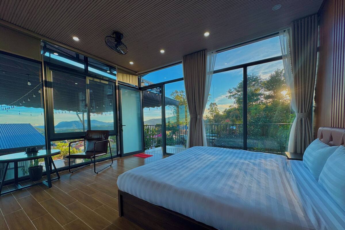Un dormitorio moderno con una cama grande, un balcón con mesa y silla, y vistas al exterior.