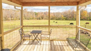 Una terraza de madera con una mesa y sillas, con vista a un potrero cercado con vacas.