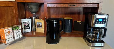 A kitchen with wooden cabinets, a coffee maker, a kettle, and various coffee pods.