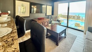 A modern living room with a marble countertop, black leather chairs, a wooden coffee table, and a large window offering a view of a pool and ocean. - Chic Condo w/ Poolside Balcony & Gulf Views. Free Golf & Daily Activities! (Panama City Beach)