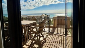 En balkon med et bord og stole, med udsigt over en strand og hav.