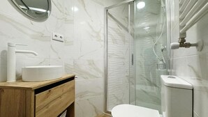 Un baño moderno con ducha envuelta en vidrio, tocador de madera con lavamanos y un inodoro.