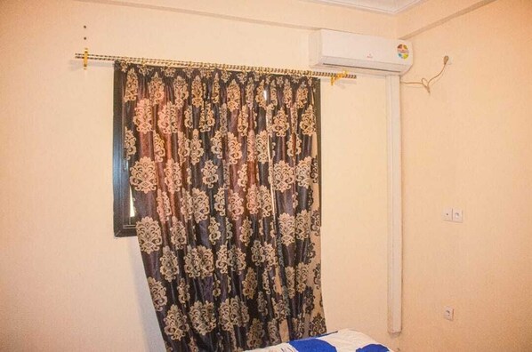A room with a bed, a curtain with a floral pattern, an air conditioning unit, and a wall-mounted light switch.