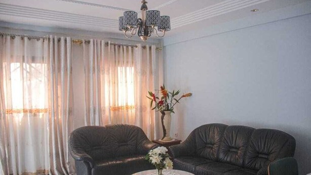 A living room with a dark leather sofa set, a round coffee table with a vase of flowers, and a chandelier.