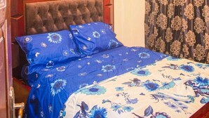 A bedroom with a tufted headboard, a floral bedspread, and a patterned curtain. - Secure apartment in the heart of yaounde 10m from the tarmac (Yaoundé)