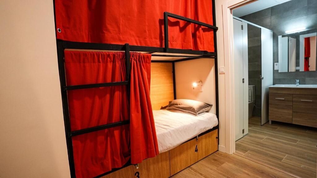 Un lit superposé avec des rideaux rouges, une lampe de chevet et un plancher en bois.