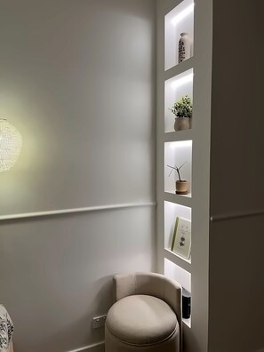 A corner of a room with a white wall, a round stool, and a shelf with decorative items. - Three-Bedroom Ocean-View (Tamarama)