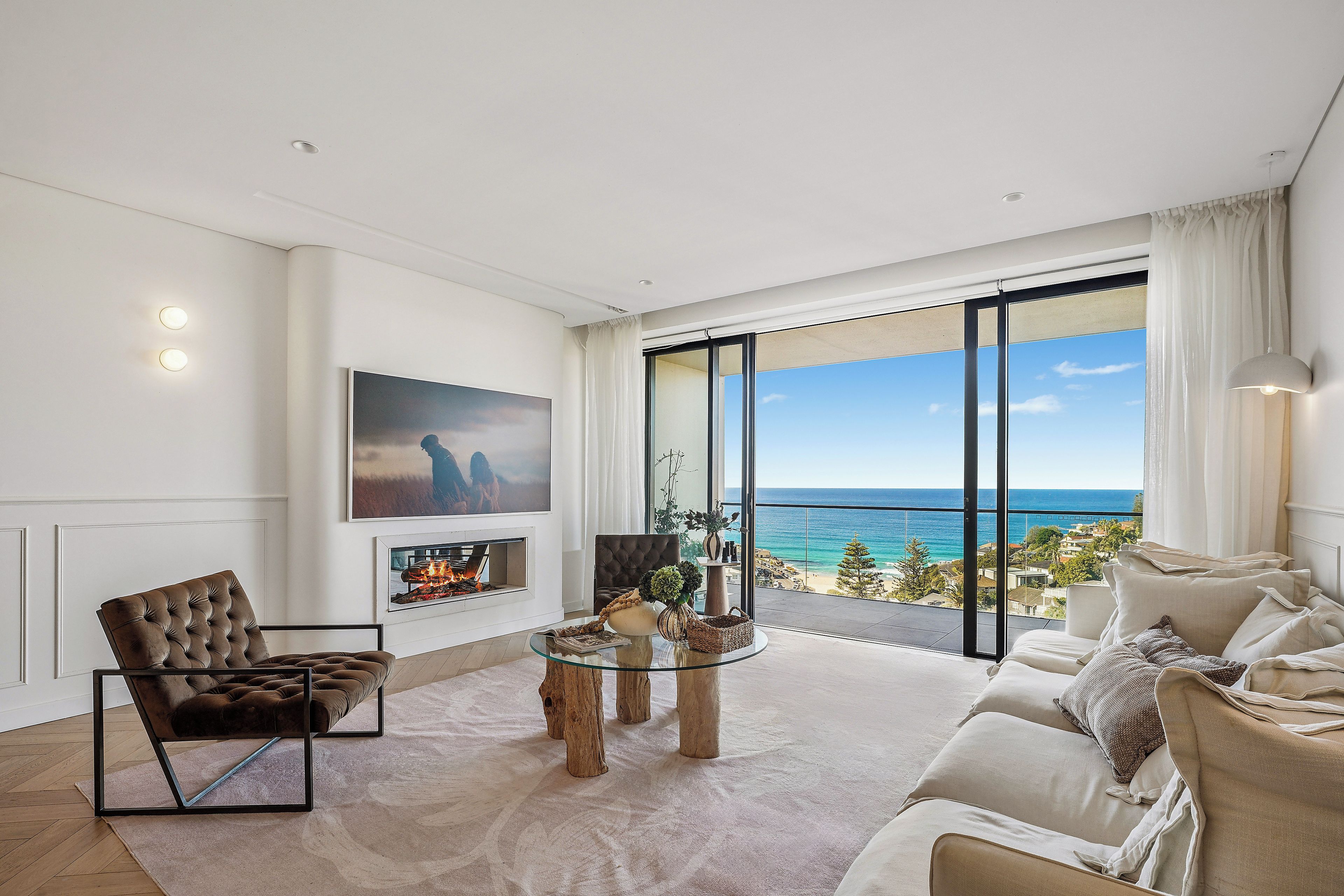 A modern living room with a fireplace, a sofa, a coffee table, and a large window offering a view of the ocean.