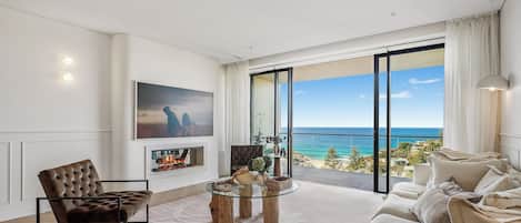 A modern living room with a fireplace, a sofa, a coffee table, and a large window offering a view of the ocean.