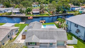 A residential area with houses, a swimming pool, and a dock extending into a body of water. - Remodeled Waterfront Home Heated Saltwater Pool & Spa With Gulf Access (New Port Richey)