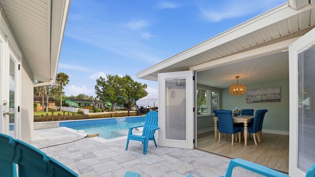 A poolside area with blue chairs, a dining table with chairs, and a view of the pool and greenery. - Remodeled Waterfront Home Heated Saltwater Pool & Spa With Gulf Access (New Port Richey)