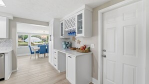 A modern kitchen with white cabinetry, a dining area with blue chairs, and a view of the outdoors. - Remodeled Waterfront Home Heated Saltwater Pool & Spa With Gulf Access (New Port Richey)