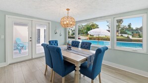 A dining area with a wooden table, blue upholstered chairs, and a hanging light fixture. - Remodeled Waterfront Home Heated Saltwater Pool & Spa With Gulf Access (New Port Richey)