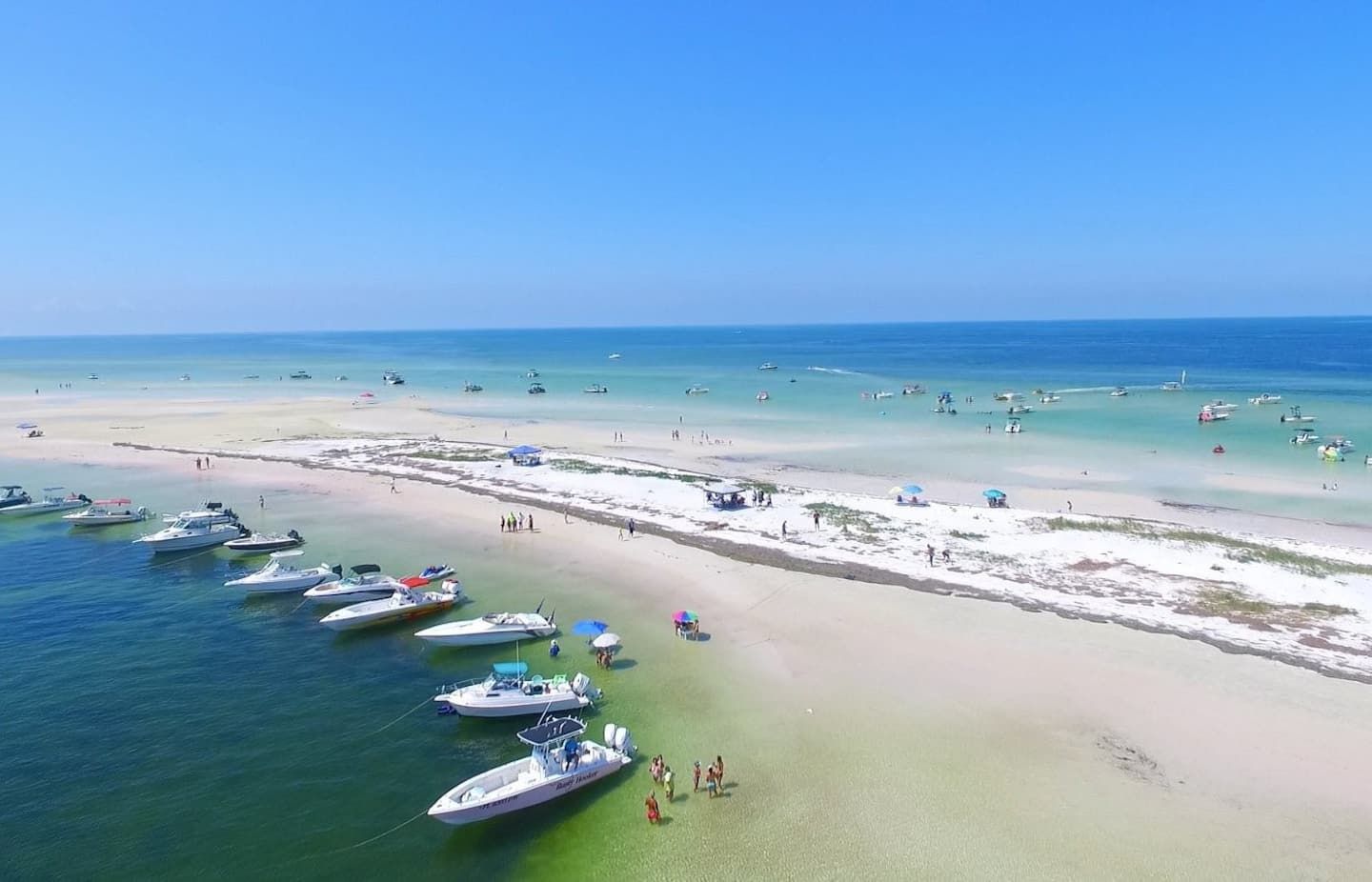 A beach with boats docked and people walking on the sand.