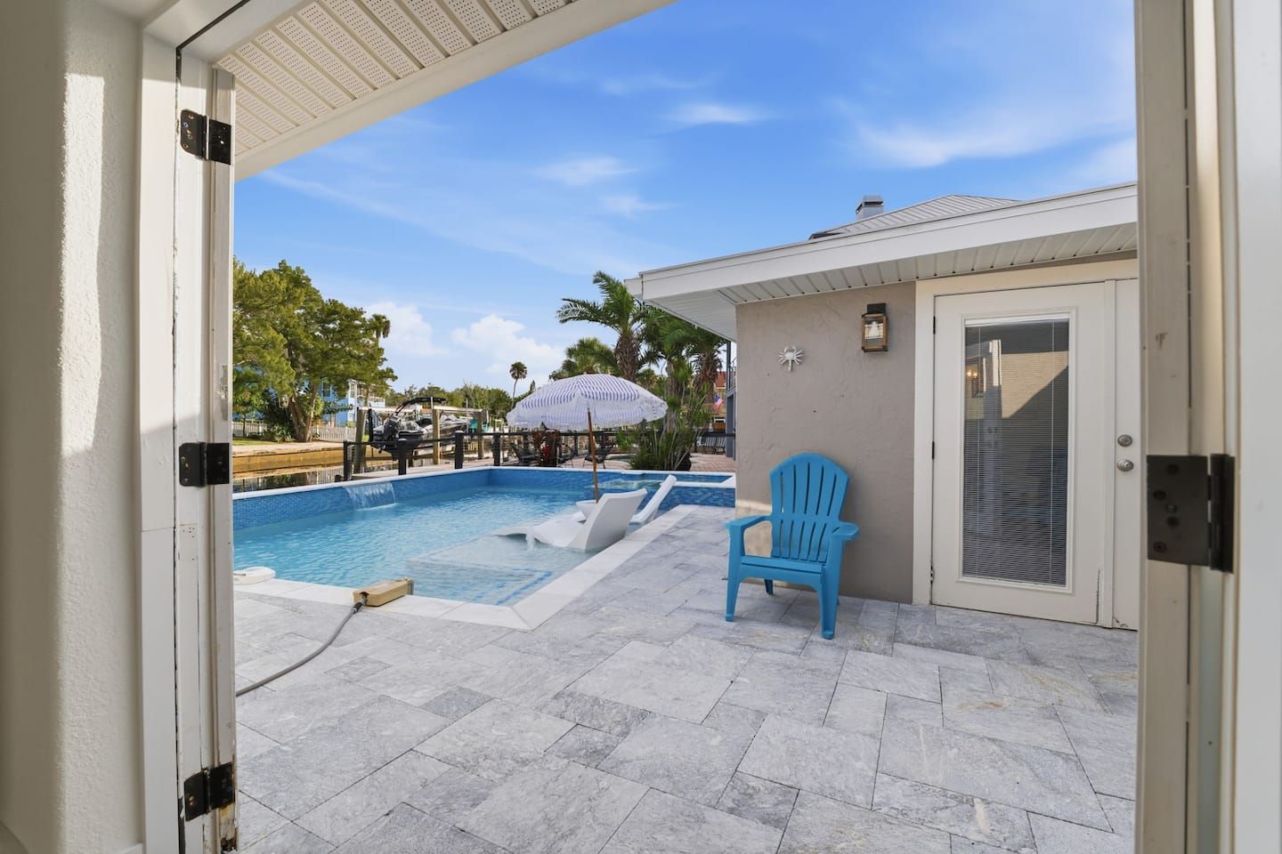 A swimming pool with a blue chair and a door leading to a covered area.