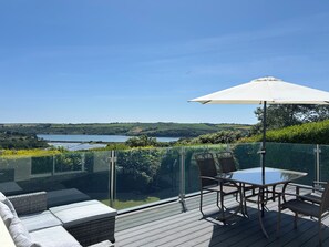 A glass-enclosed outdoor seating area with a table and chairs, overlooking a lake and hilly landscape. - Spacious home with fabulous views & hot tub, sleeps 8, 4 bedrooms. (Kinsale)