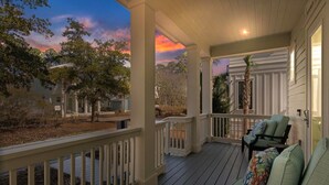 A covered porch with a view of a house and trees, a chair, and a table.