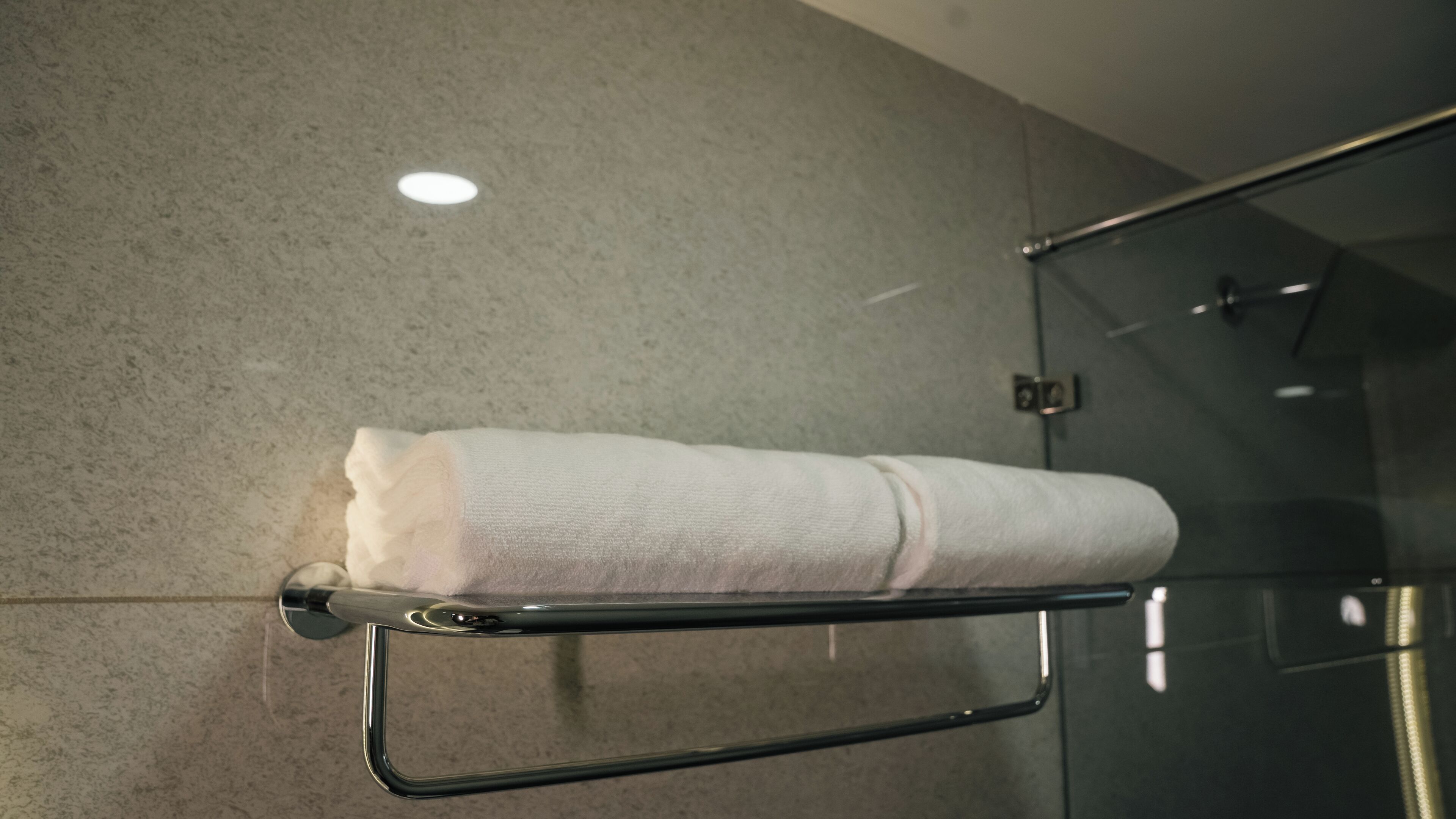 Une serviette est suspendue à un porte-serviettes en métal dans une salle de bain dotée d’une porte de douche en verre et d’un mur à texture.