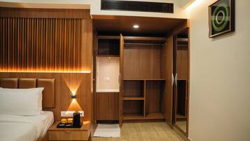 A hotel room with a bed, bedside table with a coffee maker, and a wooden wardrobe with a mirror.