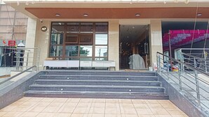 Η είσοδος του ξενοδοχείου M7 Plaza, με τη μοντέρνα πρόσοψη, μια σκάλα που οδηγεί στην είσοδο και έναν ευδιάκριτο χώρο με καθίσματα έξω.