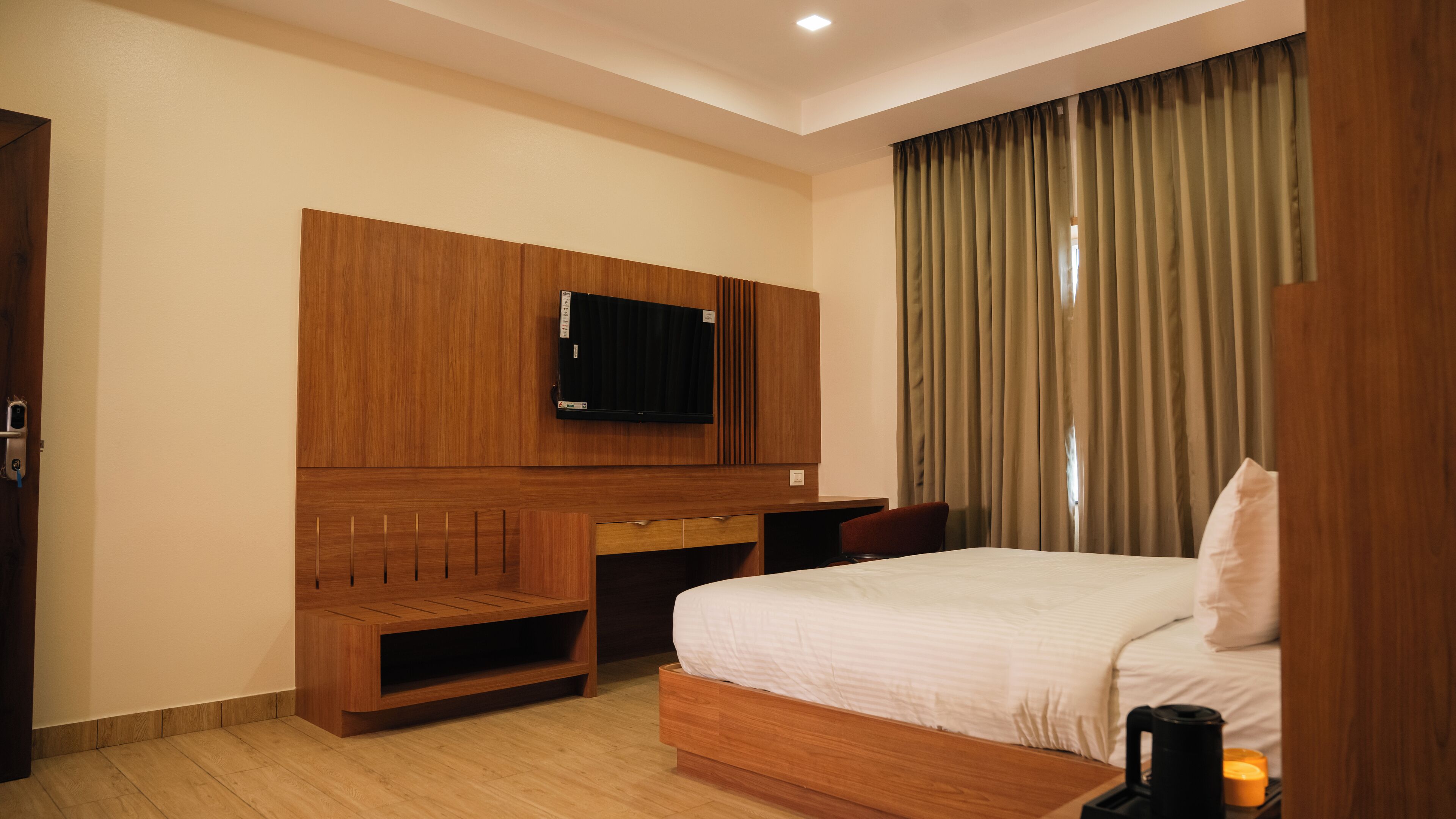 A hotel room with a bed, a TV mounted on a wooden panel, a desk, and a chair.