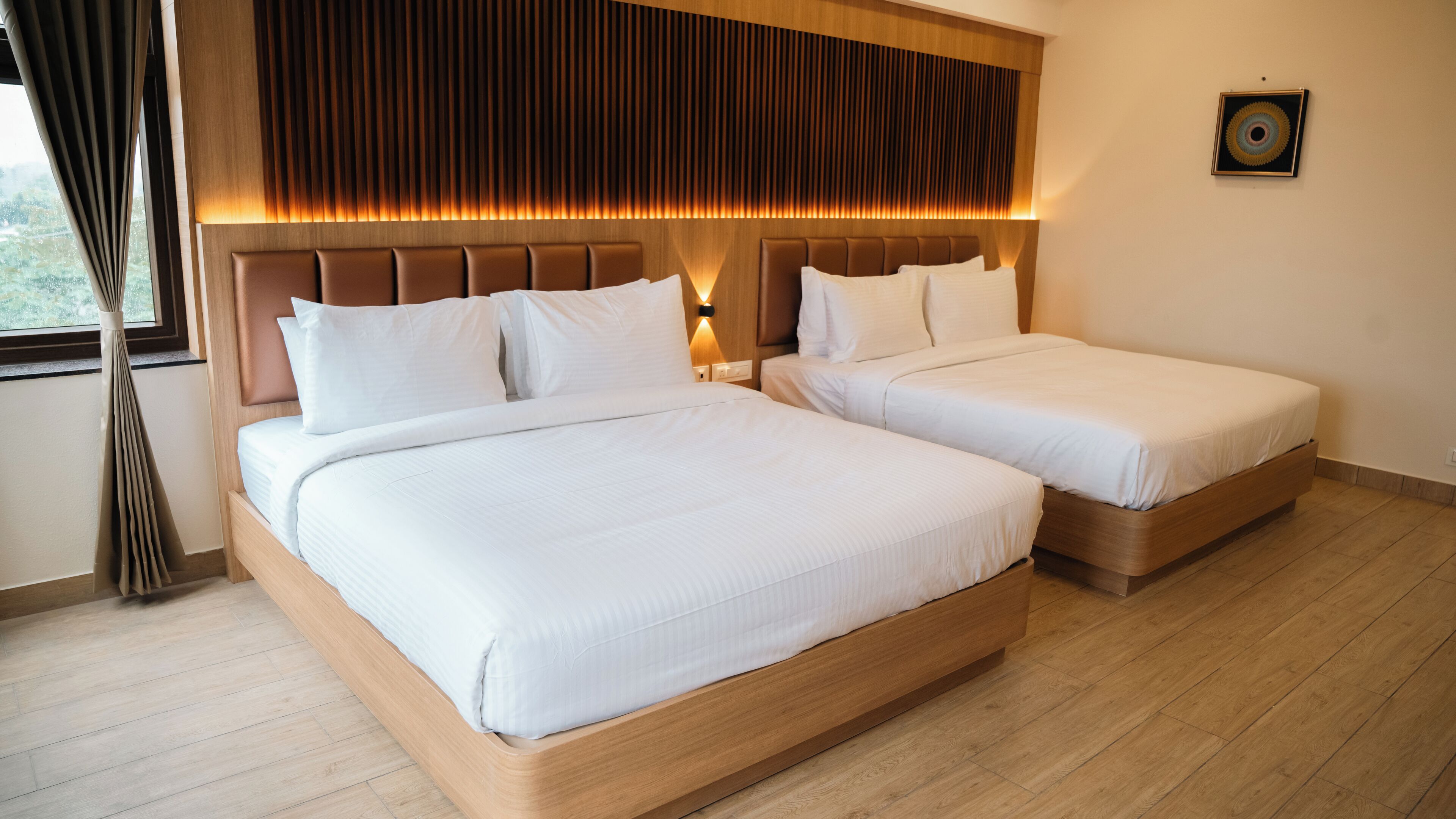 A hotel room with two beds, wooden headboards, and a large window with curtains.
