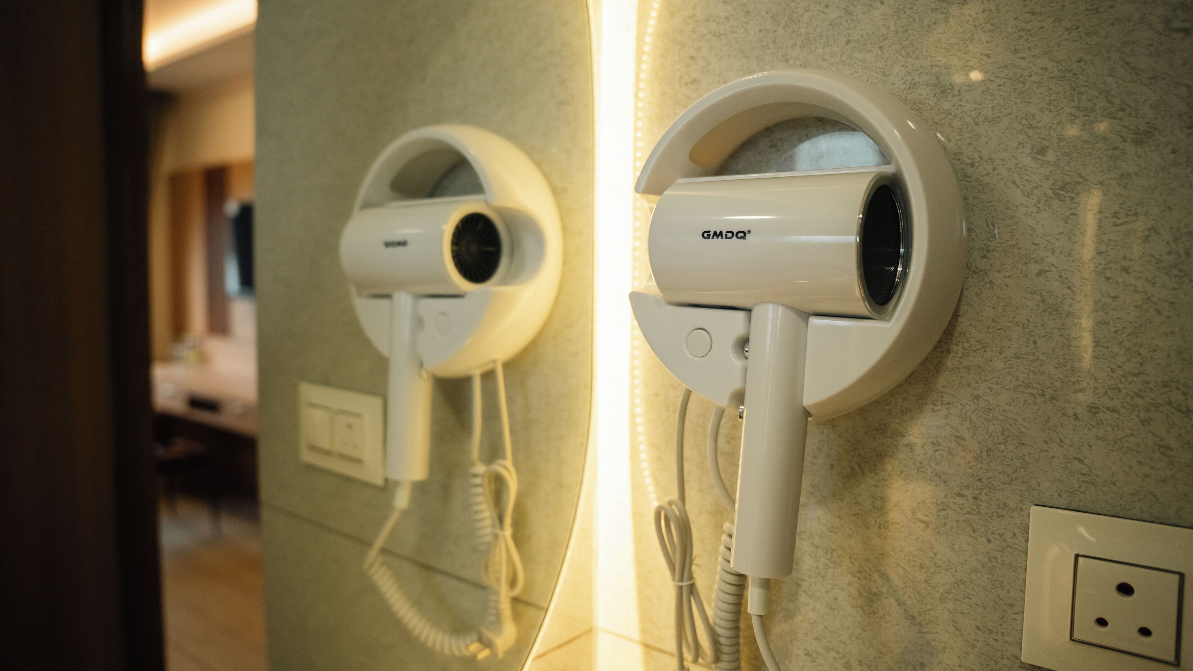 Two wall-mounted hair dryers with cords, a light switch, and a power outlet on a textured wall.