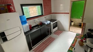 Een kleine keuken met witte kastjes, een zwart aanrecht, een raam met rode jaloezieën en een groene deur.
