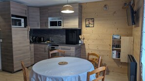 A compact kitchen with wooden cabinets, a microwave, and a dining table with chairs. - Apartment in Les Hameaux du Lay, close to the cable cars! (Les Contamines-Montjoie)